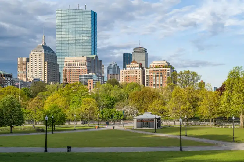 Green grass field with trees and buildings in distance under white clouds and blue sky during