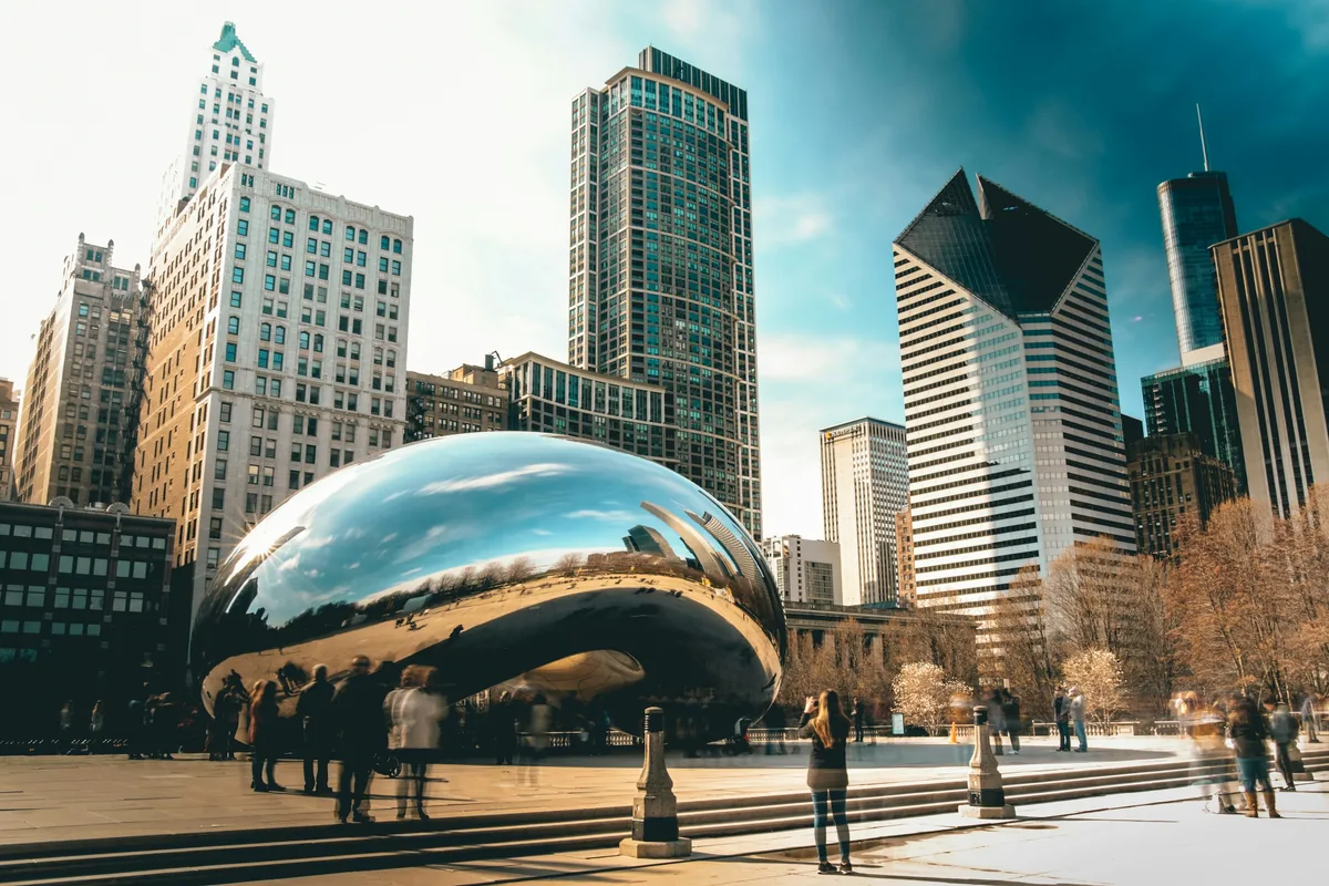 People walking around Cloud Gate sculpture in Millennium Park with Chicago skyscrapers behind