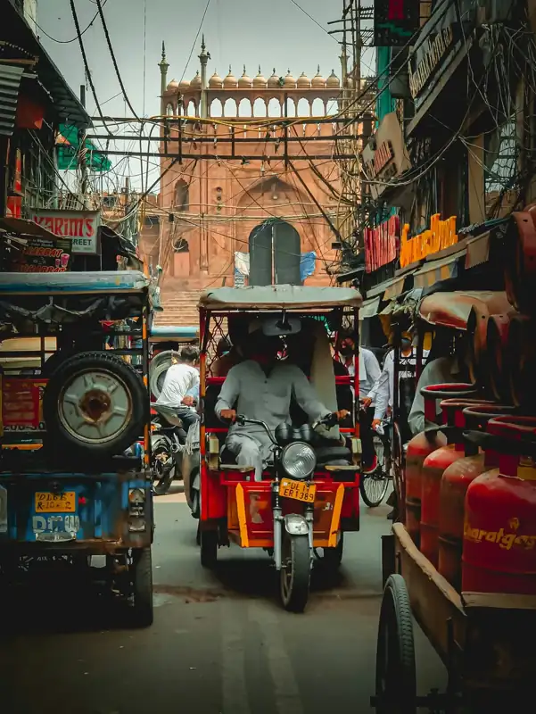 Man in black jacket riding red and black auto rickshaw