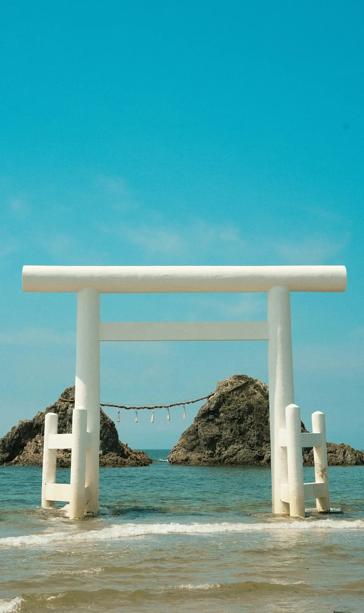 White torii gate on a beach with ocean rocks