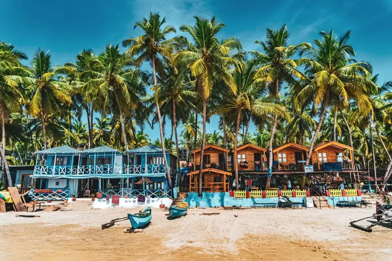 Colorful beach huts and palm trees on a sandy shore under a blue sky