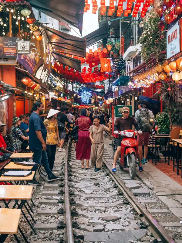 People walk on train tracks lined with restaurants and lanterns