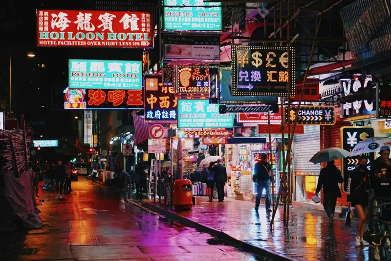 People walking on a wet city street under glowing neon signs in Hong Kong
