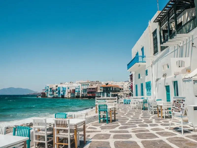 Tables and chairs on a stone patio beside the sea in Mykonos, Greece