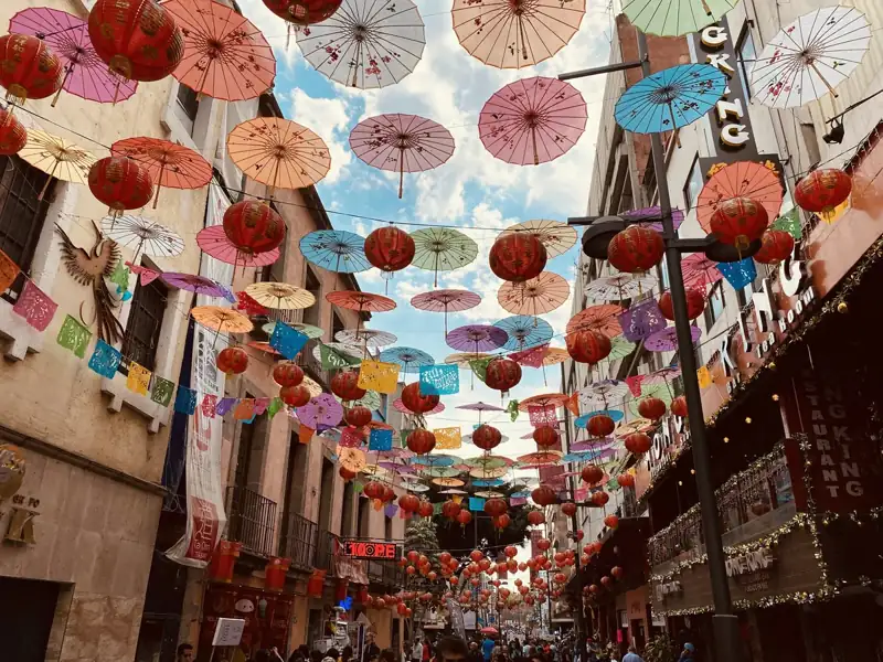 Colorful paper umbrellas and red lanterns hanging above a narrow street in Mexico City