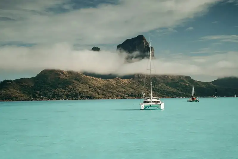 White boat on sea near mountain under white clouds during daytime