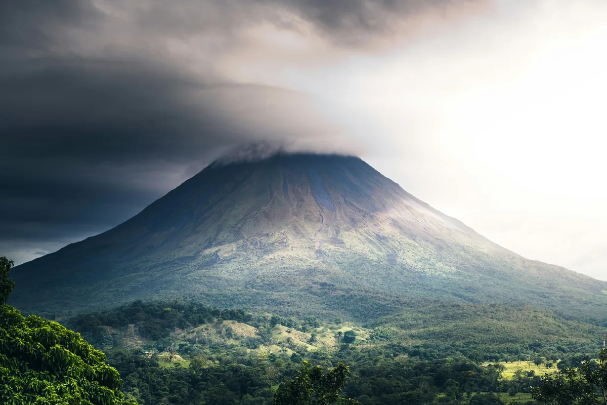 A very tall mountain with a very cloudy sky above it