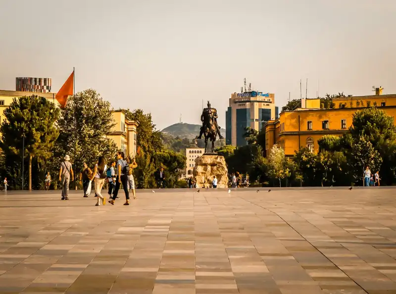 People walk in a city square with a statue