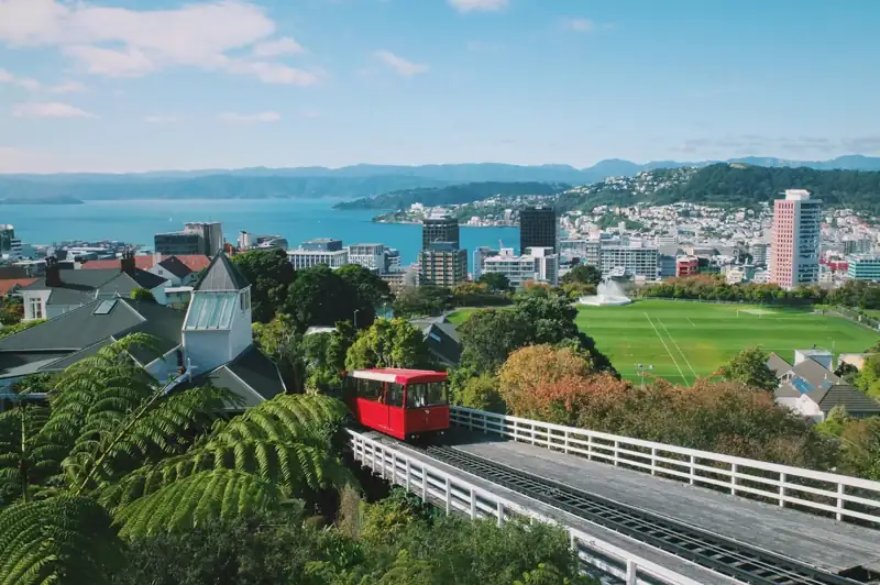 A red train traveling down tracks next to a lush green hillside