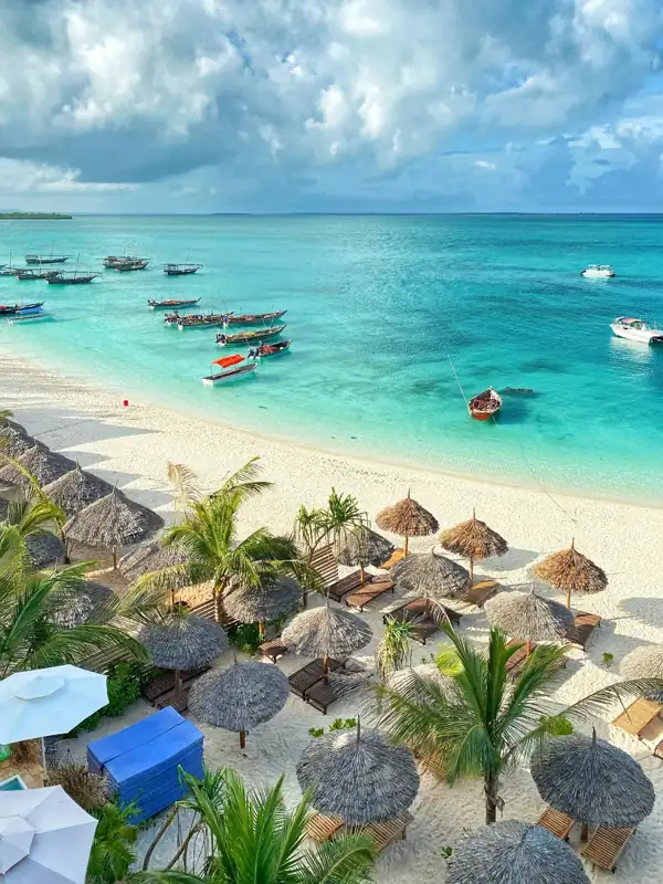 Small wooden boats anchored in turquoise water off a sandy beach with straw umbrellas